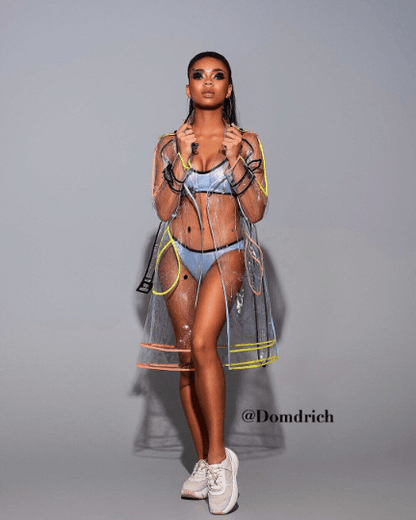 Model wearing a long transparent hooded raincoat with neon trim in a city setting.