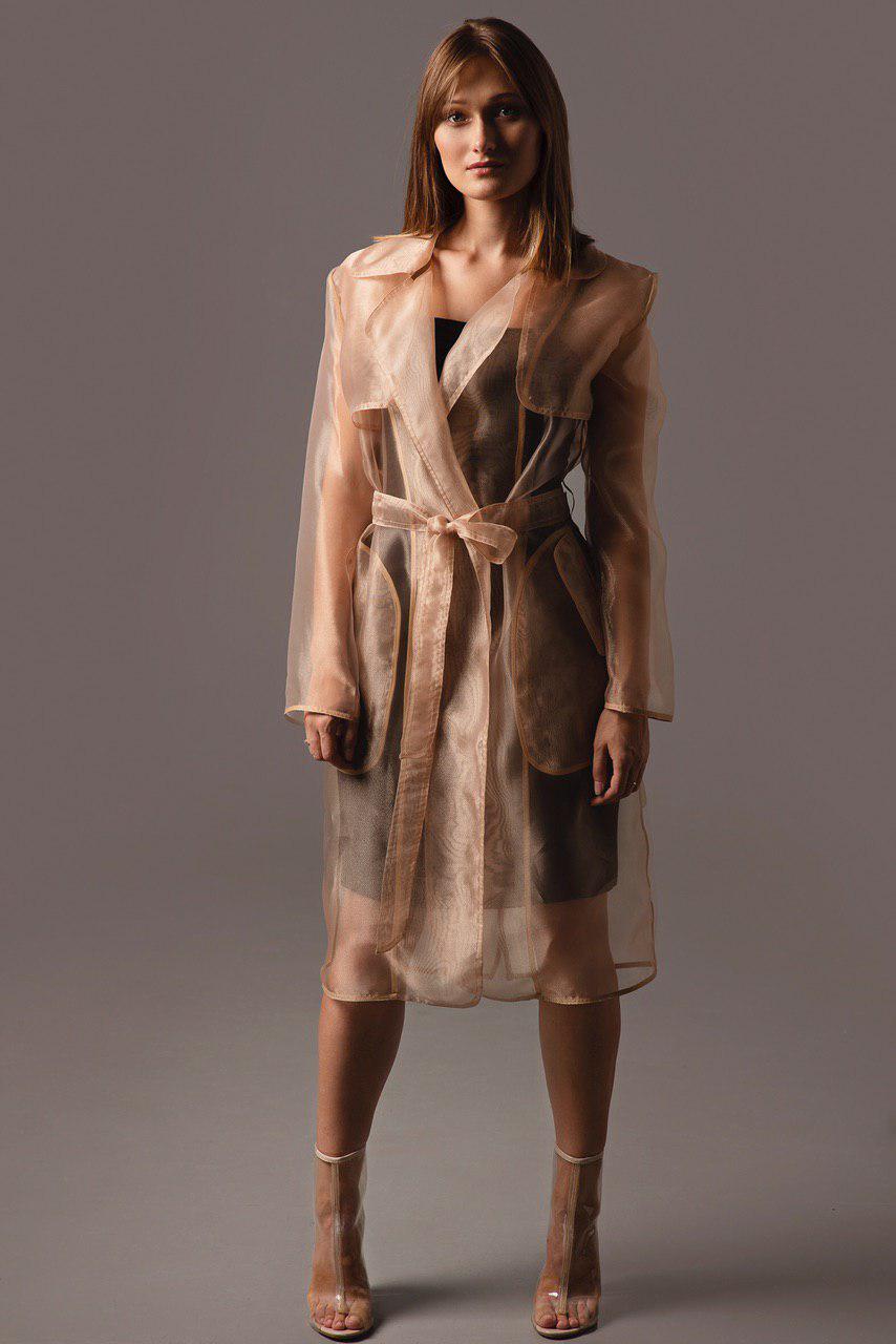 Woman wearing a sheer beige trench coat against a gray background
