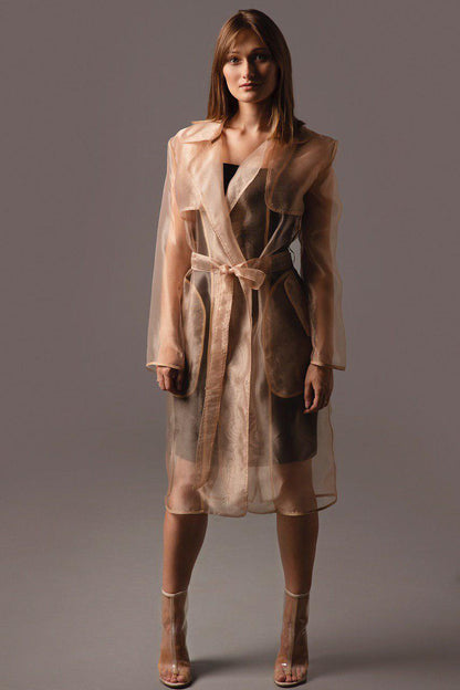 Woman wearing a sheer beige trench coat against a gray background